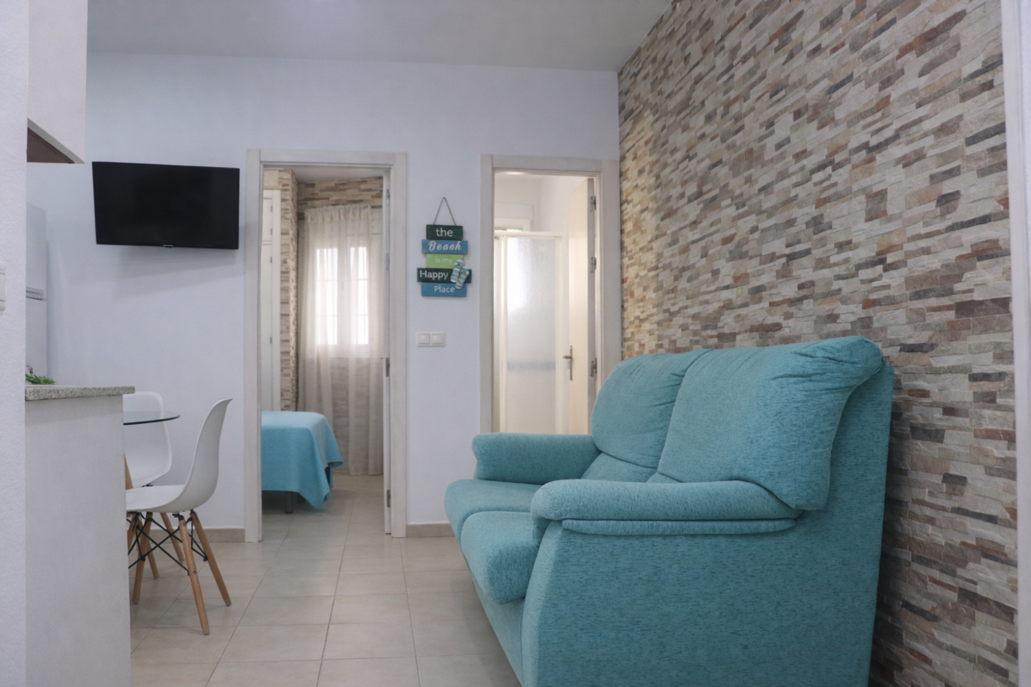 Salón con sofá turquesa y pared de piedra del Apartamento Playa Azul