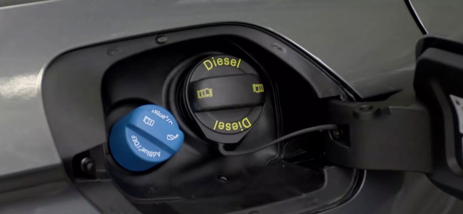 Blue AdBlue filler cap next to the black diesel cap under a vehicle's fuel flap